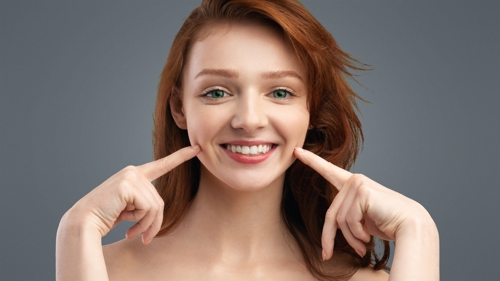 Image of a woman pointing to the dimples on her cheeks.