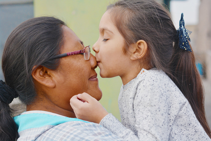 A Native American girl kisses her mother on the nose.