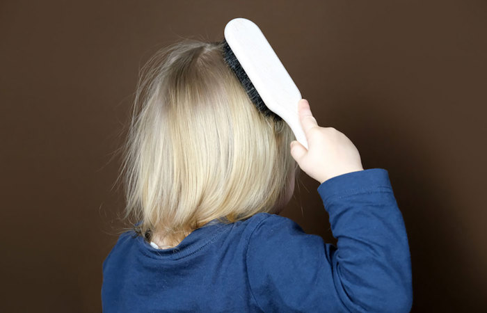 A blonde child brushing their hair.
