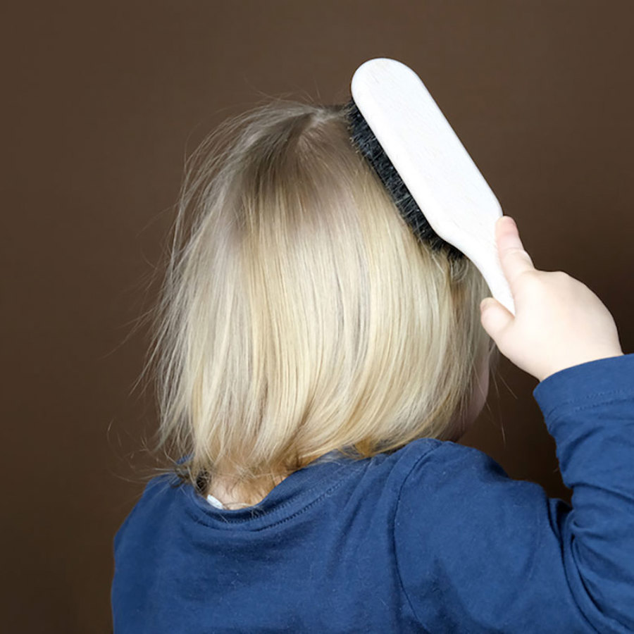 A blonde child brushing their hair.