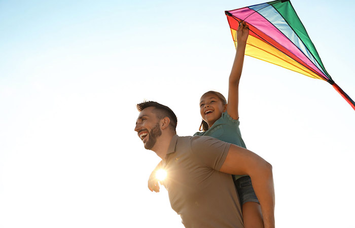 Father and daughter flying a rainbow-colored kite.
