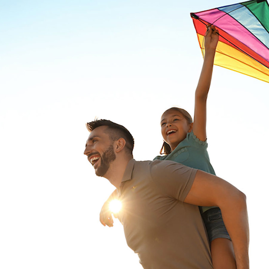 Father and daughter flying a rainbow-colored kite.