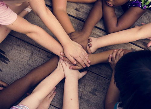 A group of children with diverse skin tones putting their hands together.