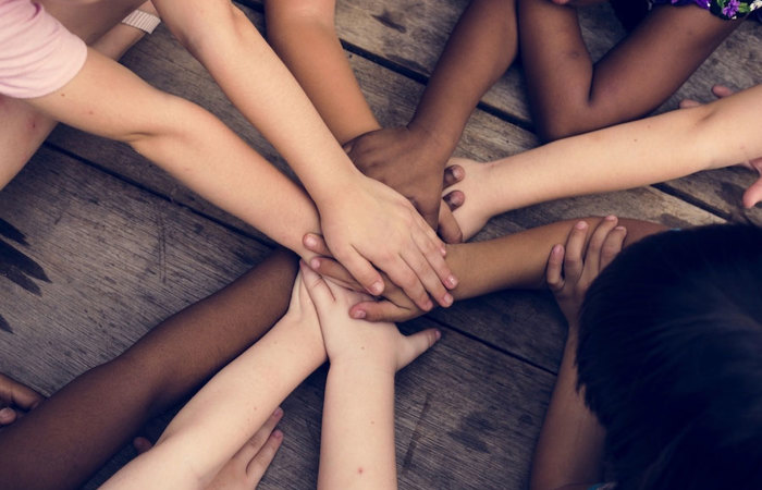 A group of children with diverse skin tones putting their hands together.