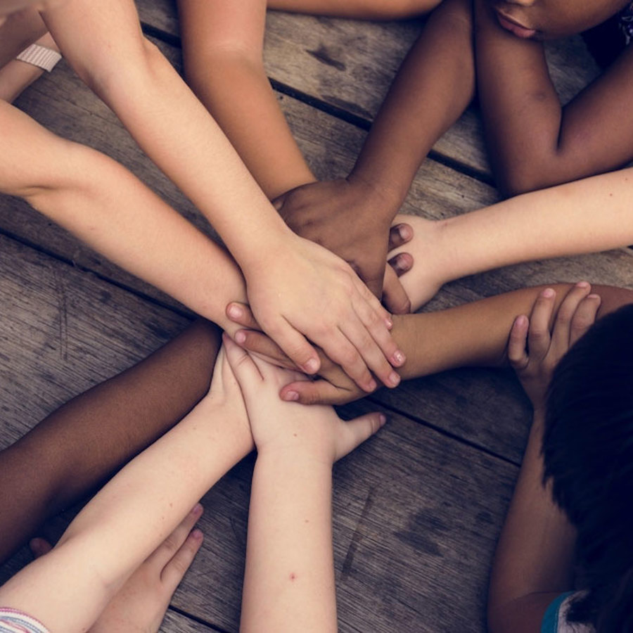 A group of children with diverse skin tones putting their hands together.