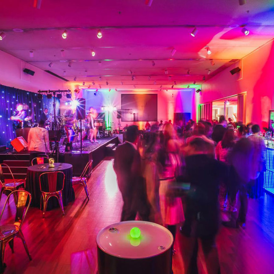 New Venture Hall transformed with colorful uplights, a decorated stage, and full bar for a corporate event.