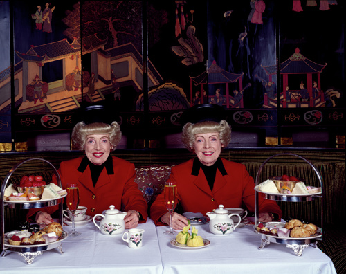 Image of two smiling identical twins mirroring each other at a tea party.