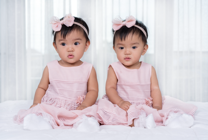 Identical twin toddlers wearing identical pink dresses.