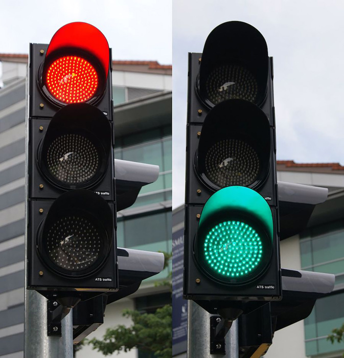 A side-by-side view of two traffic lights. One indicating a red traffic signal and the other a green traffic signal.